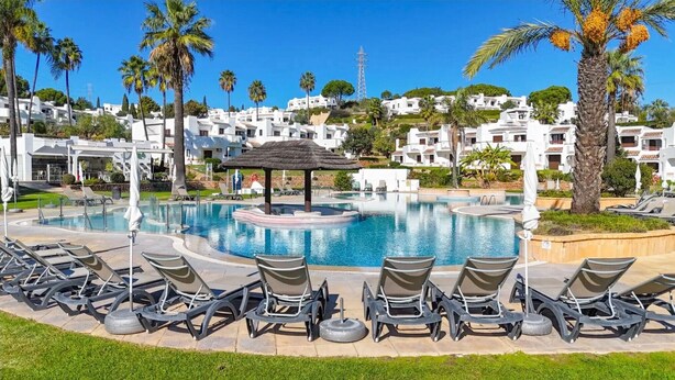 A pool area with lounge chairs, a central water feature, and white buildings in the background. - Holiday Apartment in Albufeira Resort with Check-in, Terrace, and Pools (Albufeira)