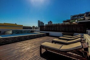 A rooftop with a pool, lounge chairs, and a view of the city skyline.