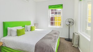 A hotel room with a bed, a window with curtains, a standing fan, and a radiator. - Luxury 2 Bedroom With Roof Deck and Pool Dewaterkant (Cape Town)