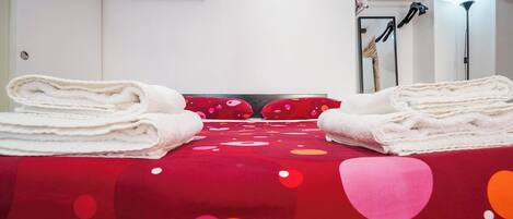 A hotel room with a red bedspread, two towels on the bed, a framed picture on the wall, and a mirror with a towel rack.