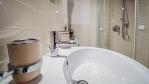 Un baño con lavamanos blanco, grifo cromado y cabina de ducha de vidrio.