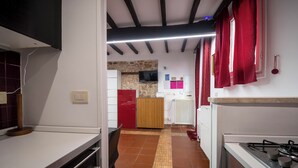 Una cocina estrecha con suelo de baldosas, estufa a gas, un armario de madera y una cortina roja.