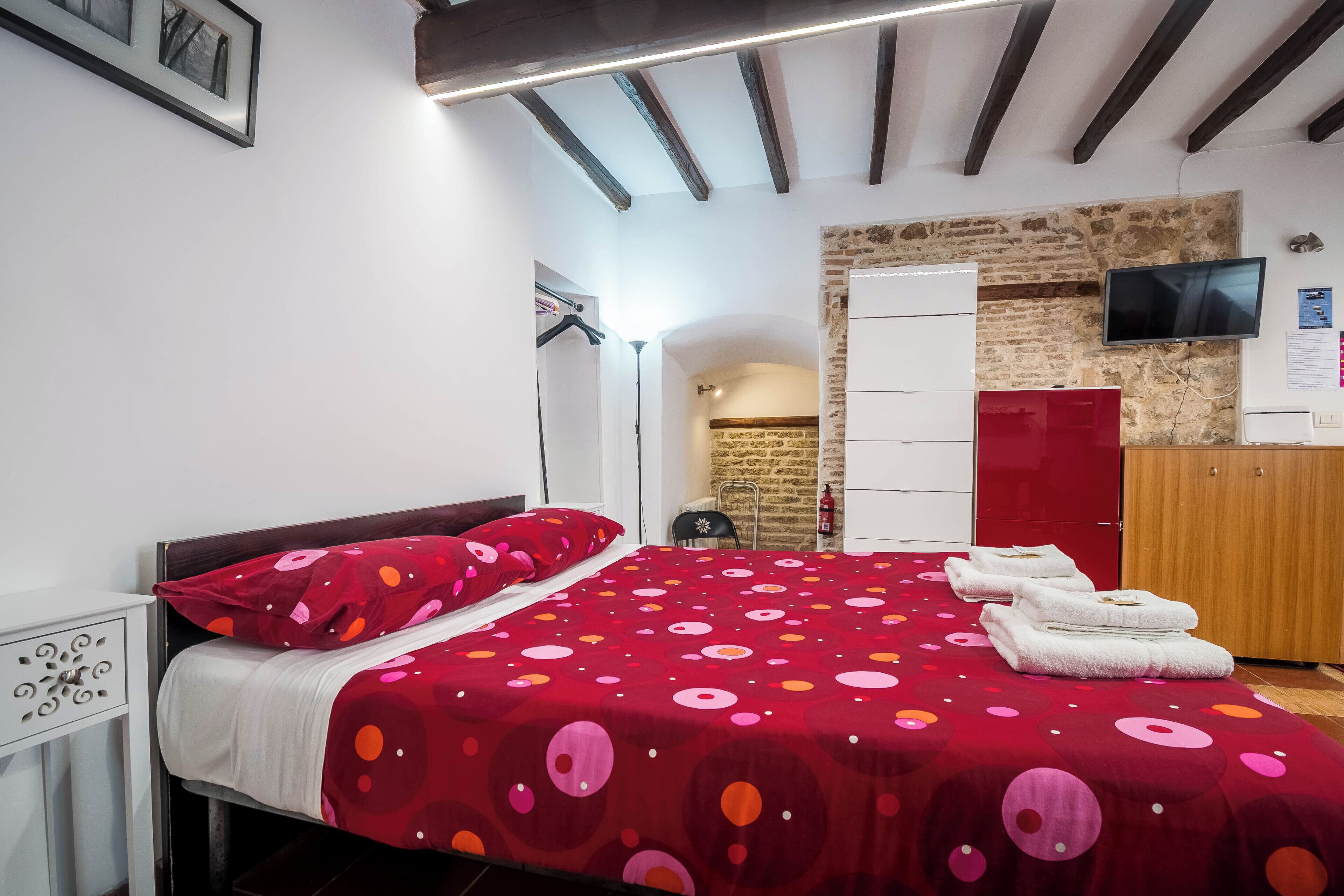 A bedroom with a bed, a wardrobe, a television, and a stone wall.