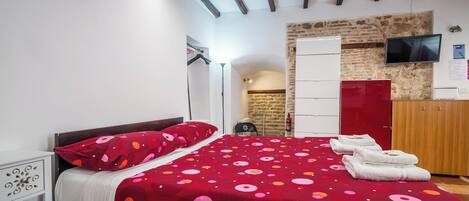 A bedroom with a bed, a wardrobe, a television, and a stone wall.