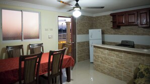 A kitchen with a dining table and chairs, a refrigerator, and a ceiling fan. - 1-bedroom Apartment With 3 Beds & Private Balcony Near SDQ Airport Fast Wi-f (Santo Domingo Este)