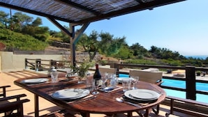 A wooden table set for dining with a view of a swimming pool and a mountainous landscape. - Alonissos 4-bedroom Large Villa With Private Pool (Alonissos)