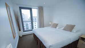 Une chambre d’hôtel avec un grand lit, une fenêtre avec des rideaux, une table de chevet et une vue sur les bâtiments environnants.