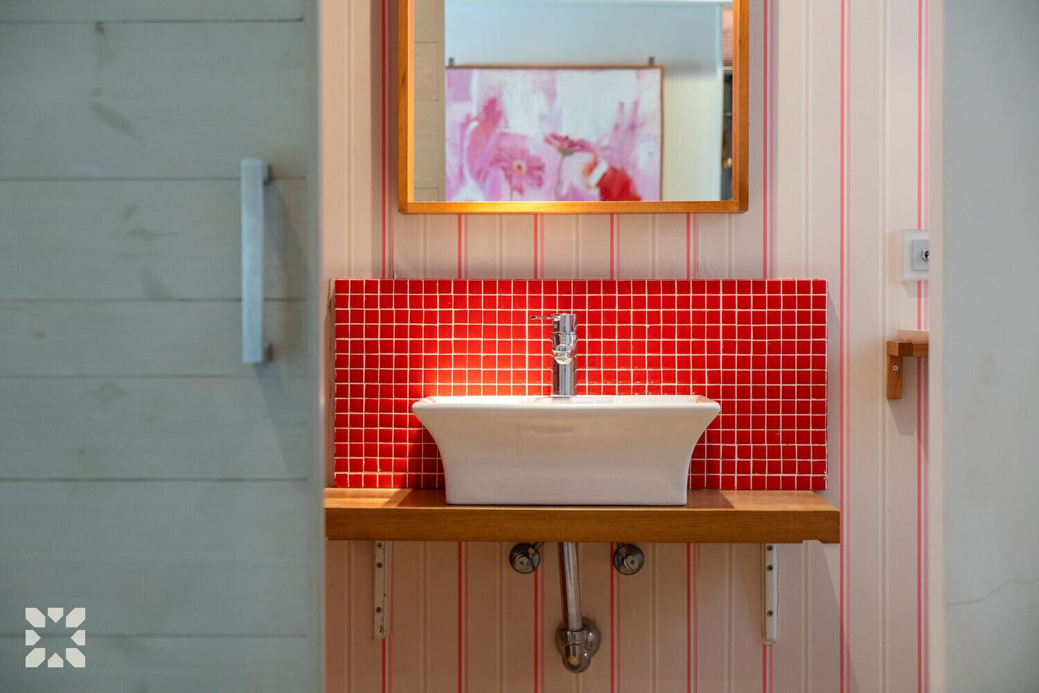 A bathroom with a white sink, red tiled backsplash, and a wooden countertop.