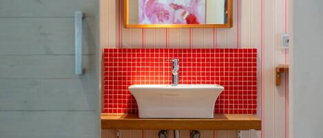 A bathroom with a white sink, red tiled backsplash, and a wooden countertop.