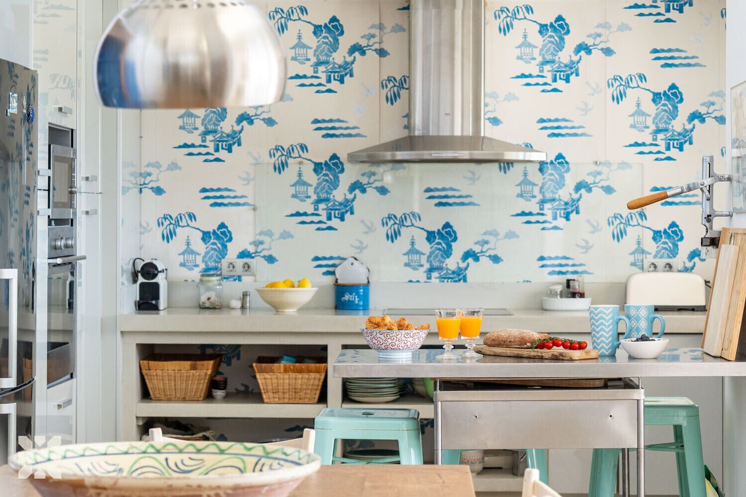 Eine Küche mit blau-weißer Tapete, einem Edelstahl-Dunstabzug, einem Toaster, einer Obstschale und einer Kaffeemaschine.