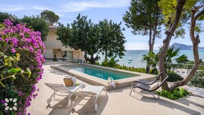 Zona de piscina con sillones, una mesa con una bebida y vista al mar.
