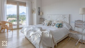Un dormitorio con una cama grande, un balcón con vistas a las montañas y una silla de mimbre.