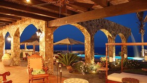 An outdoor patio area with stone arches, wooden furniture, and a view of the ocean at dusk. - Relax by Your Private Pool, San Jose Del Cabo 1041 (San Jose Del Cabo)