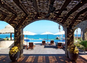 A covered outdoor seating area with a view of the ocean, stone pillars, and umbrellas. - Relax by Your Private Pool, San Jose Del Cabo 1041 (San Jose Del Cabo)