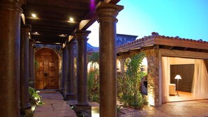 A covered outdoor area with stone columns, a wooden door, and a building with a tiled roof. - Relax by Your Private Pool, San Jose Del Cabo 1041 (San Jose Del Cabo)
