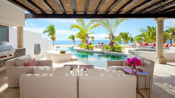 Un espace aménagé au bord de la piscine, avec vue sur l’océan, des sièges d’extérieur et un barbecue.
