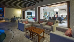 Un espace de vie extérieur moderne, doté de canapés et de tables en bois, qui est relié à un espace intérieur lumineux comprenant un coin repas et une cuisine.