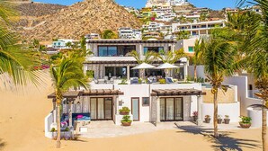 Une propriété moderne située en bord de mer, dotée d’une piscine, d’un espace extérieur aménagé et de palmiers.