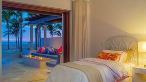 Une chambre à coucher avec un lit, une table de chevet et une vue sur une plage au crépuscule.