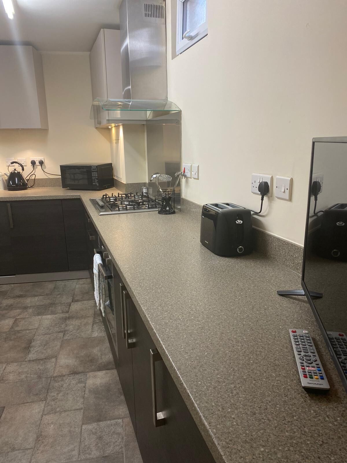 A kitchen with a granite countertop, a gas stove, a microwave, a toaster, and a kettle.