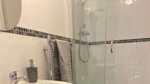 Une salle de bain avec un lavabo blanc, une cabine de douche en verre et un tapis à motifs sur le sol.