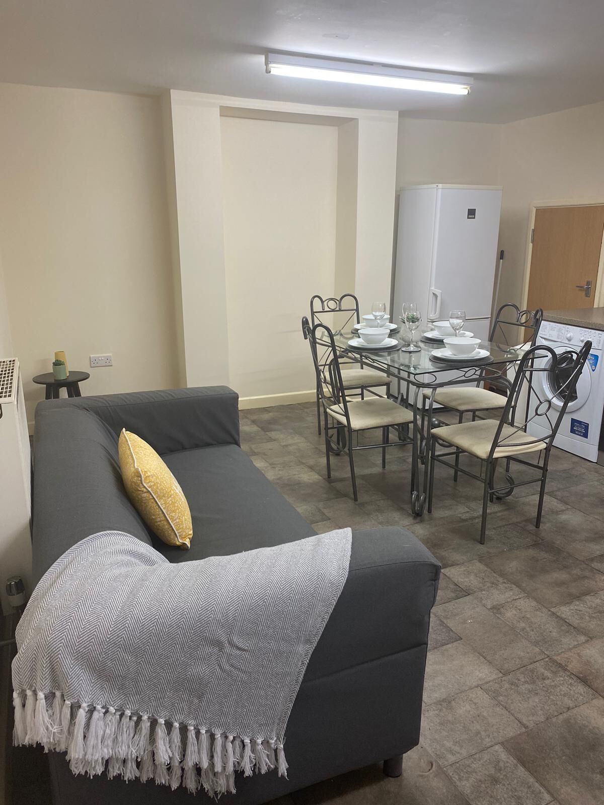 Un espace de vie compact comprenant un canapé, une table à manger pour quatre personnes et un lave-linge.