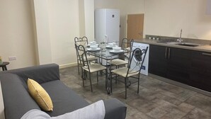 Un espace de vie compact comprenant une table à manger pour quatre personnes, un canapé avec des coussins, un lave-linge et une kitchenette équipée d’un évier et d’un plan de travail.