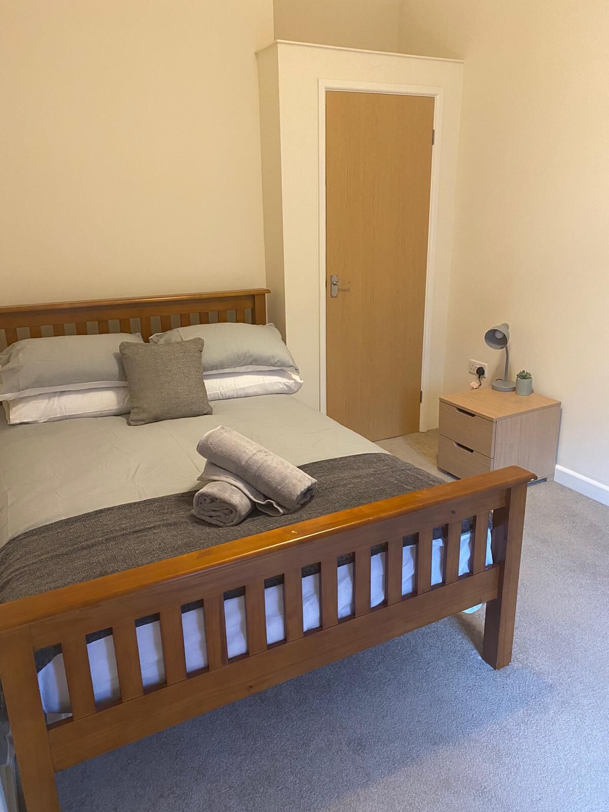Un dormitorio con una cama de madera, una mesita de noche con lámpara y un armario.