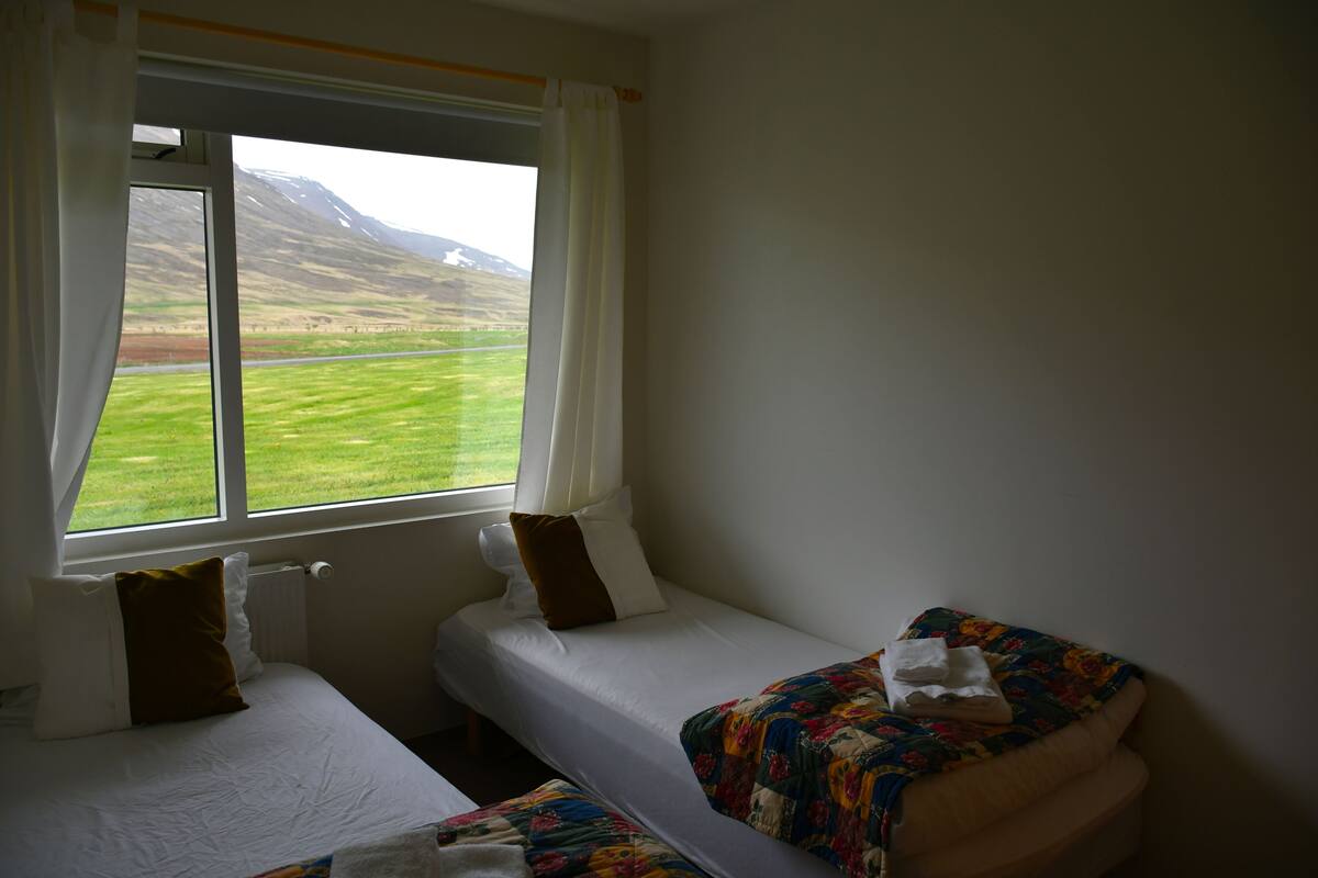 Ein Zimmer mit zwei Betten, einem Vorhangfenster und Blick auf eine grüne Landschaft.
