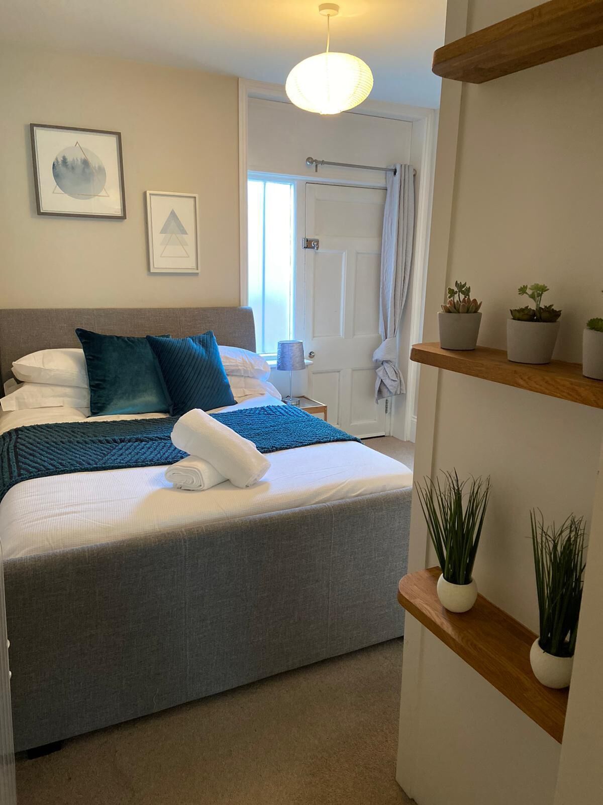 A neatly arranged bedroom with a bed, pillows, a bedside table, a lamp, and wall art.