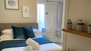 Een keurig opgemaakt slaapkamer met een bed, kussens, een nachtkastje, een lamp en wanddecoratie.
