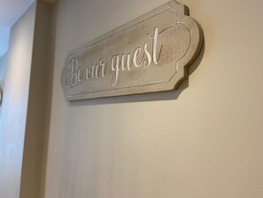 Un letrero de madera con el texto 'Sean nuestros invitados' colgado en una pared.