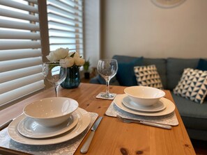 Una mesa de comedor dispuesta con cuencos, platos y cubiertos blancos, un florero con flores blancas y una copa.