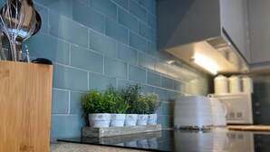 Een keuken met een blauwe betegelde spatwand, een houten snijplank en een plank met potplanten.