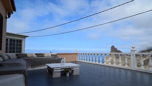 Une terrasse sur le toit, dotée d’une balustrade blanche, d’une table blanche agrémentée d’une plante en pot, et offrant une vue sur une côte rocheuse.