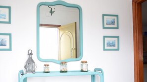 Une salle de bain avec un mur blanc, un meuble-lavabo bleu, un miroir et une porte donnant sur une autre pièce.