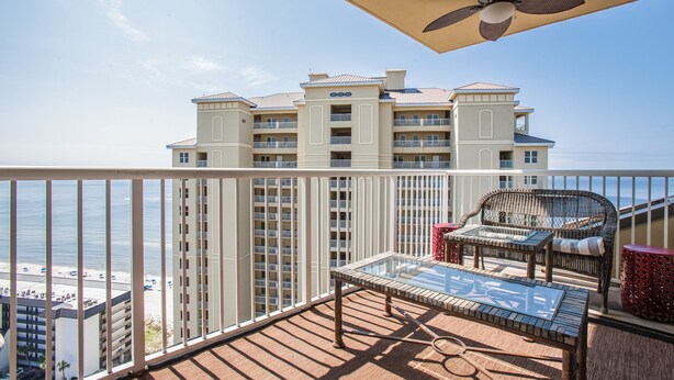A balcony with a glass-top table, wicker chairs, and a ceiling fan.