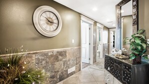 A hallway with a round wall clock, a potted plant, and a marble-tiled floor.