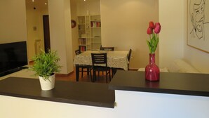 A dining area with a table, chairs, a bookshelf, and a TV in the background. - PortonHouse (Roma)