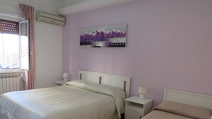 A bedroom with two beds, a radiator, a window with curtains, a wall-mounted air conditioner, and a painting. - PortonHouse (Roma)