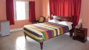 Een slaapkamer met een bed, rode gordijnen, een nachtkastje en een lamp.
