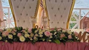 A table set for a wedding with two ornate chairs, a pink tablecloth, and a floral arrangement.