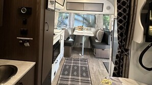 Interior compacto de una caravana con kitchenette, comedor y litera.