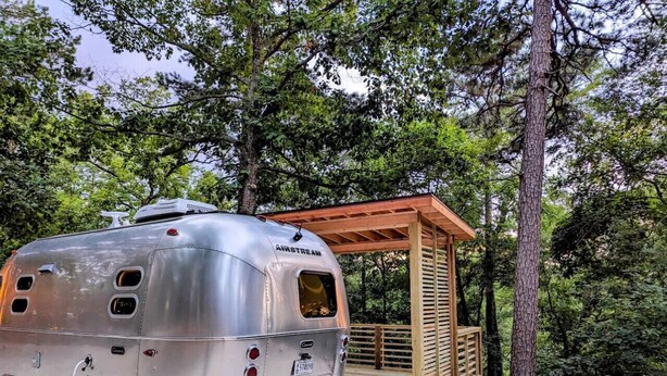 Un remolque plateado con cubierta de madera y una pequeña estructura tipo cabaña.