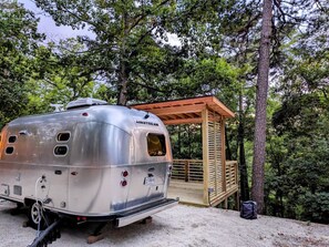 A silver trailer with a wooden deck and a small cabin-like structure.