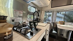 Una cocina compacta con estufa a gas, cafetera y un pequeño comedor con mesa y sillas.