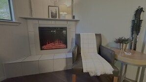 Ein Wohnzimmer mit Kamin, einer Couch, einem Tisch mit Lampe und einer Topfpflanze.