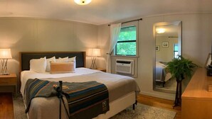 A bedroom with a bed, bedside lamps, a window with curtains, a mirror, and a plant.