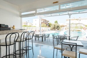 Un área de piscina interior con vista a la piscina exterior, bar y zona de estar.