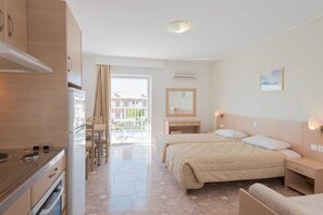 Habitació d'hotel amb zona de cuina, un llit amb edredó beix, una taula de nit, un mirall i vista a l'exterior.